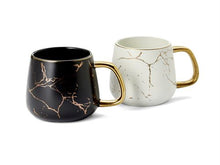 Two mugs, one black with gold accents and one white with gold accents, on a white background.