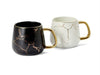 Two mugs, one black with gold accents and one white with gold accents, on a white background.