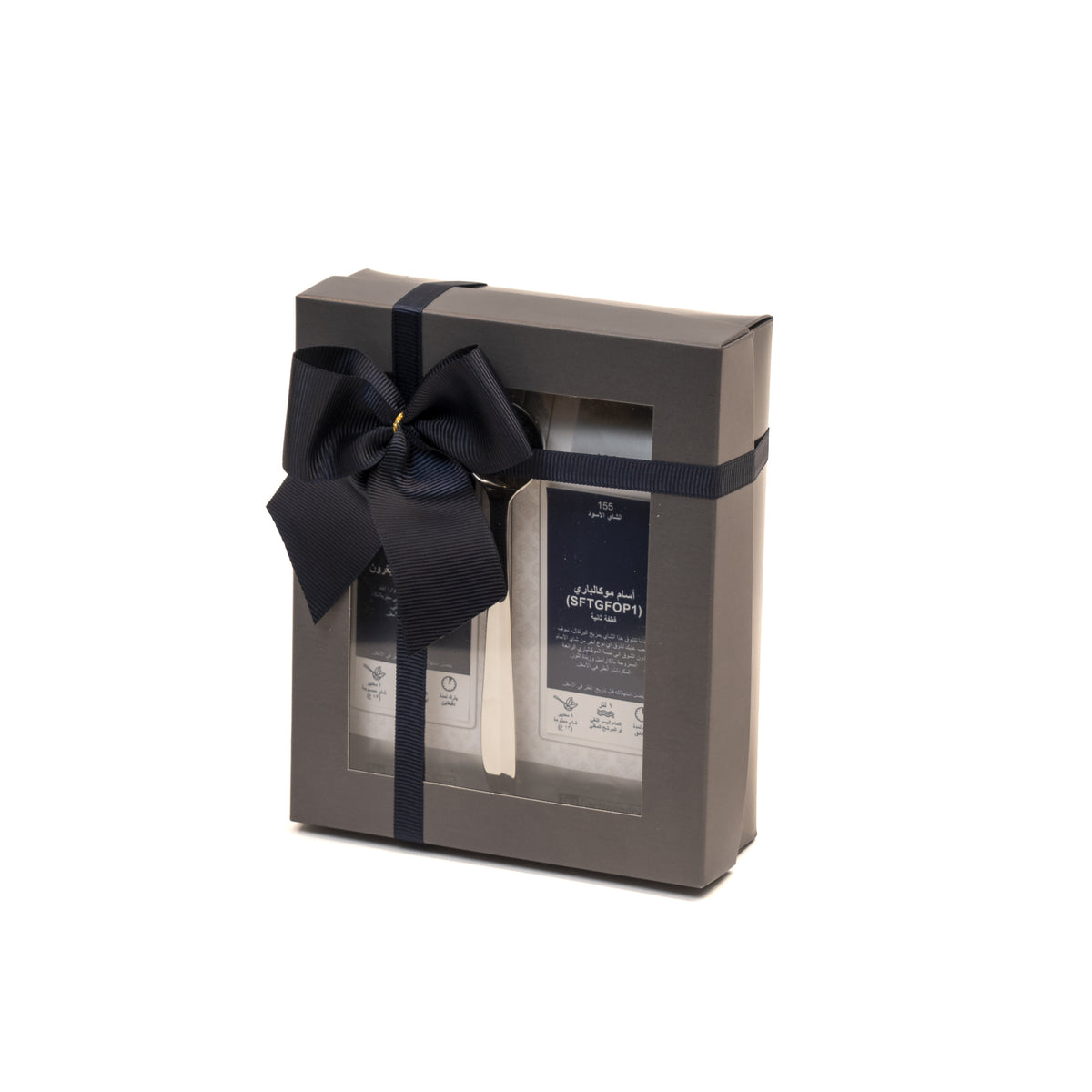 A gift tray containing two packets of black tea leaves, one labeled Assam Mokalbari and the other Ceylon OP UVA Badulla, tied with a navy blue ribbon.