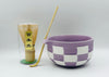 Checkered purple and white bowl with a transparent container and wooden spoon on a light gray background