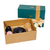 A tea gift set displayed in an open kraft paper box, with its matching teal and gold gift box behind it on a dark table against a patterned wall.