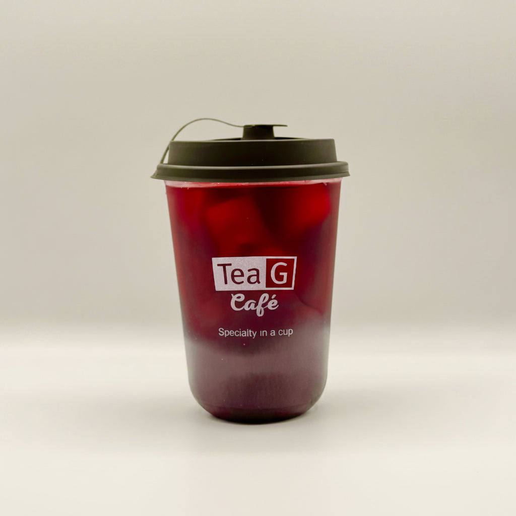 A reusable plastic takeaway cup filled with a dark red beverage, featuring a black lid with a carry loop and the white printed logo 'Tea G Cafe' on the front, set against a plain light gray background.