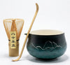 Tea-making set with a green ceramic bowl, wooden whisk, and bamboo whisk holder on a white background